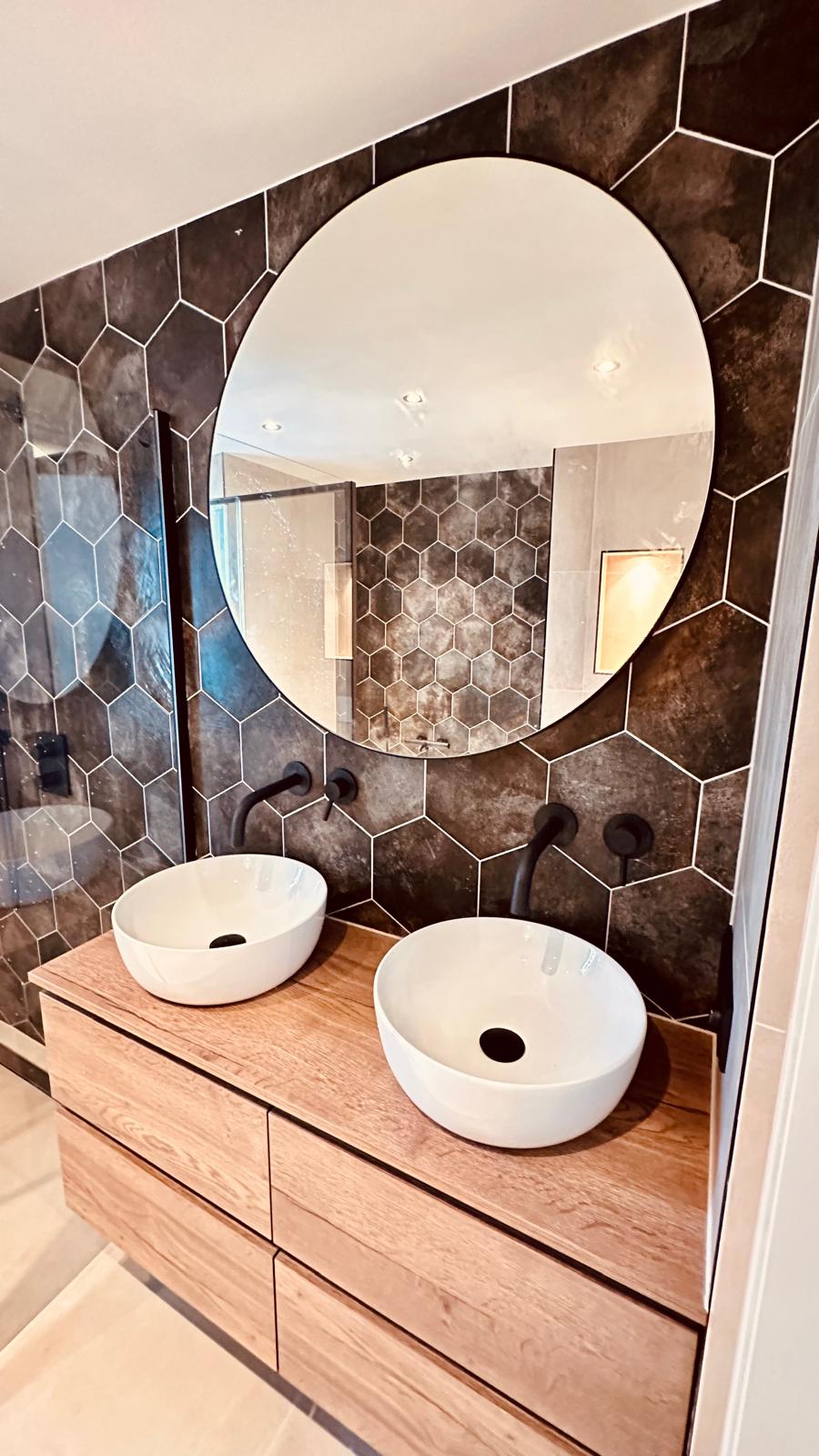 Badkamer met grote ronde spiegel, houten wastafelmeubel en hexagontegels